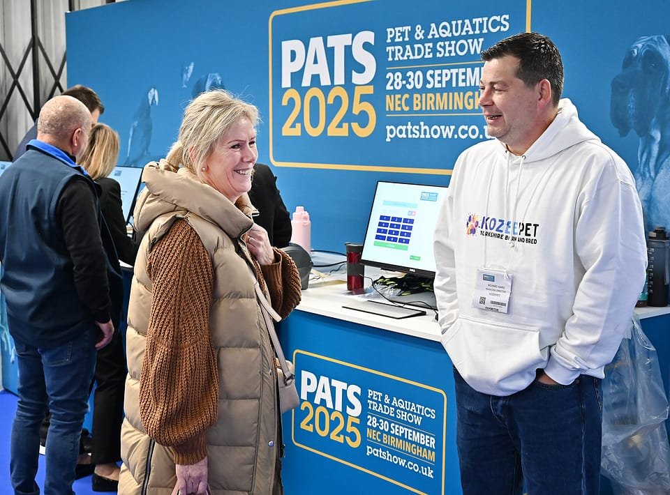 Figure 3. The PATS 2025 information desk — dates, venue and show identity clearly displayed. A KozeePet team member in branded kit talks to a visitor. Field photo from the author's on-site collection, PATS 2025.